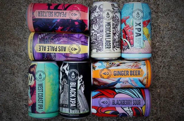 Eight beer cans laid flat in a grid on rough grey concrete, each wrapped in a different brightly coloured illustration. The labels read Peach Seltzer, Aus Pale Ale, West Coast IPA, Black XPA, Mexican Lager, XPA, Ginger Beer and Blackberry Sour.