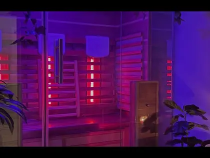 A timber-lined sauna cabin lit magenta and violet, its glass door open. Slatted pale wood walls carry glowing red heater panels and two rounded white fixtures, with a bench along the back. Leafy plants stand in the foreground and a candle burns on a small table at the right.