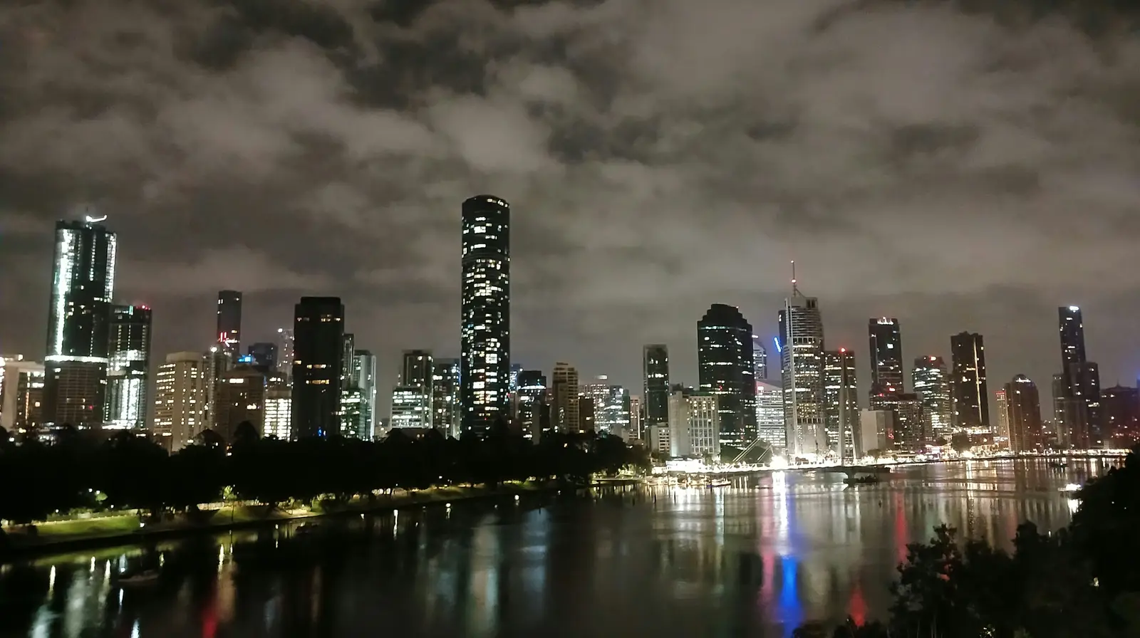 Brisbane's lit skyline at night across the river from Kangaroo Point, tower lights reflected in the water under heavy cloud
