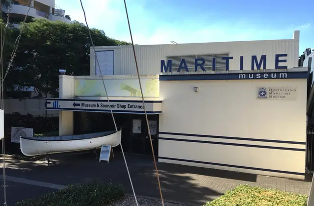 The museum's cream entrance building with large blue MARITIME museum lettering along the top, a white timber lifeboat on a cradle beside the doorway and a sign pointing to the museum and souvenir shop.
