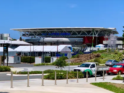 The arena's long cantilevered white roof carrying blue PAT RAFTER ARENA lettering, with white event marquees and a tall wire sculpture set up on the forecourt in front of it.