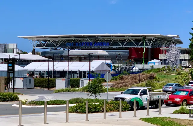 The arena's long cantilevered white roof carrying blue PAT RAFTER ARENA lettering, with white event marquees and a tall wire sculpture set up on the forecourt in front of it.